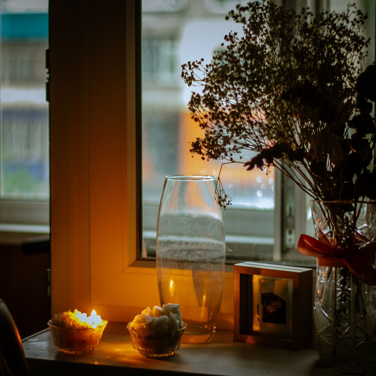 Intérieur intime avec bougies et fleurs près d'une fenêtre, ambiance de recueillement chaleureuse